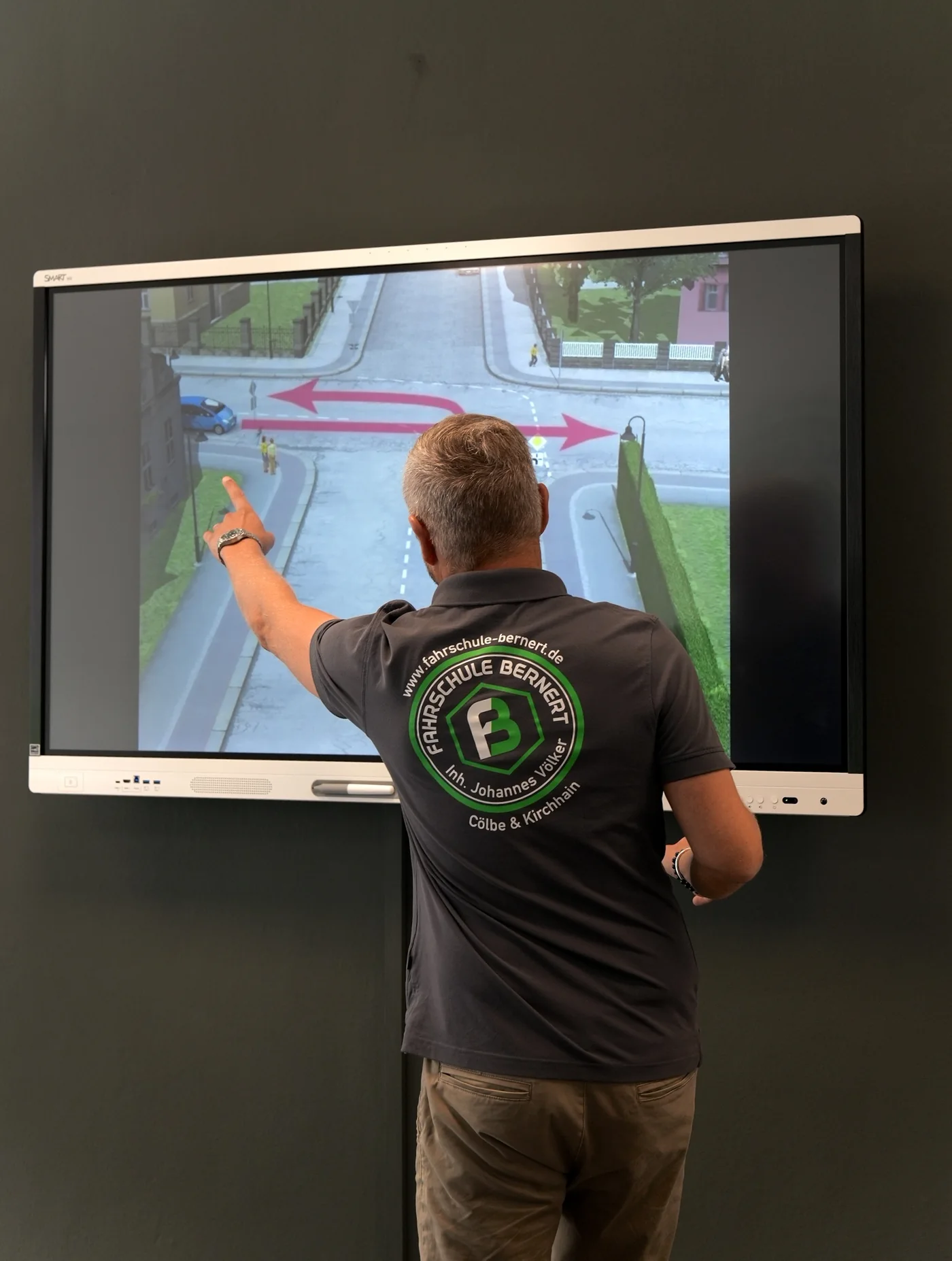 Fahrlehrer erklärt eine Verkehrssituation am Bildschirm im Theorieraum